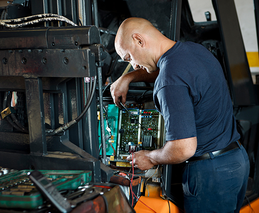 A mechanic examining the wires of a forklift